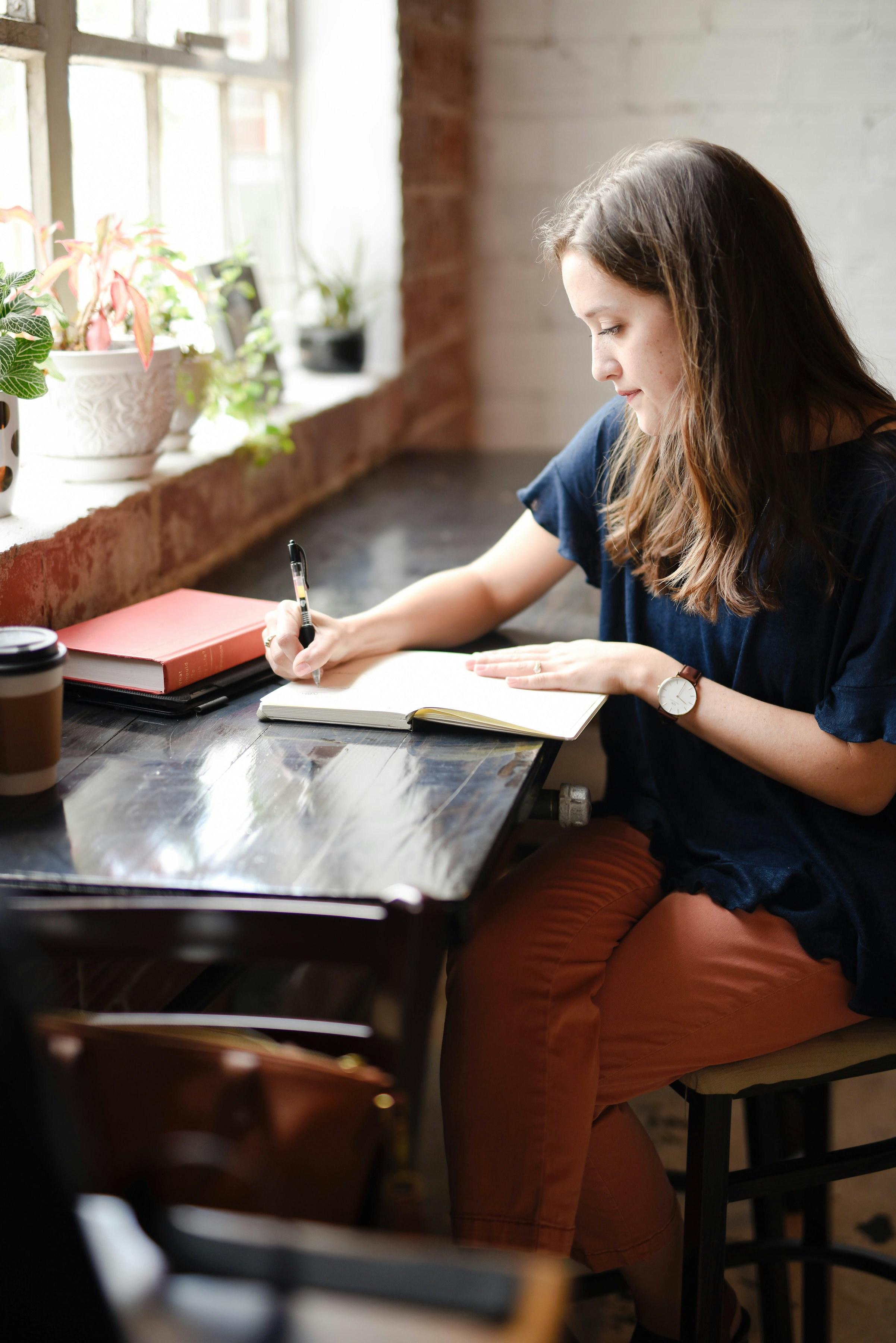 A woman writing thoughtfully in a notebook beside a window