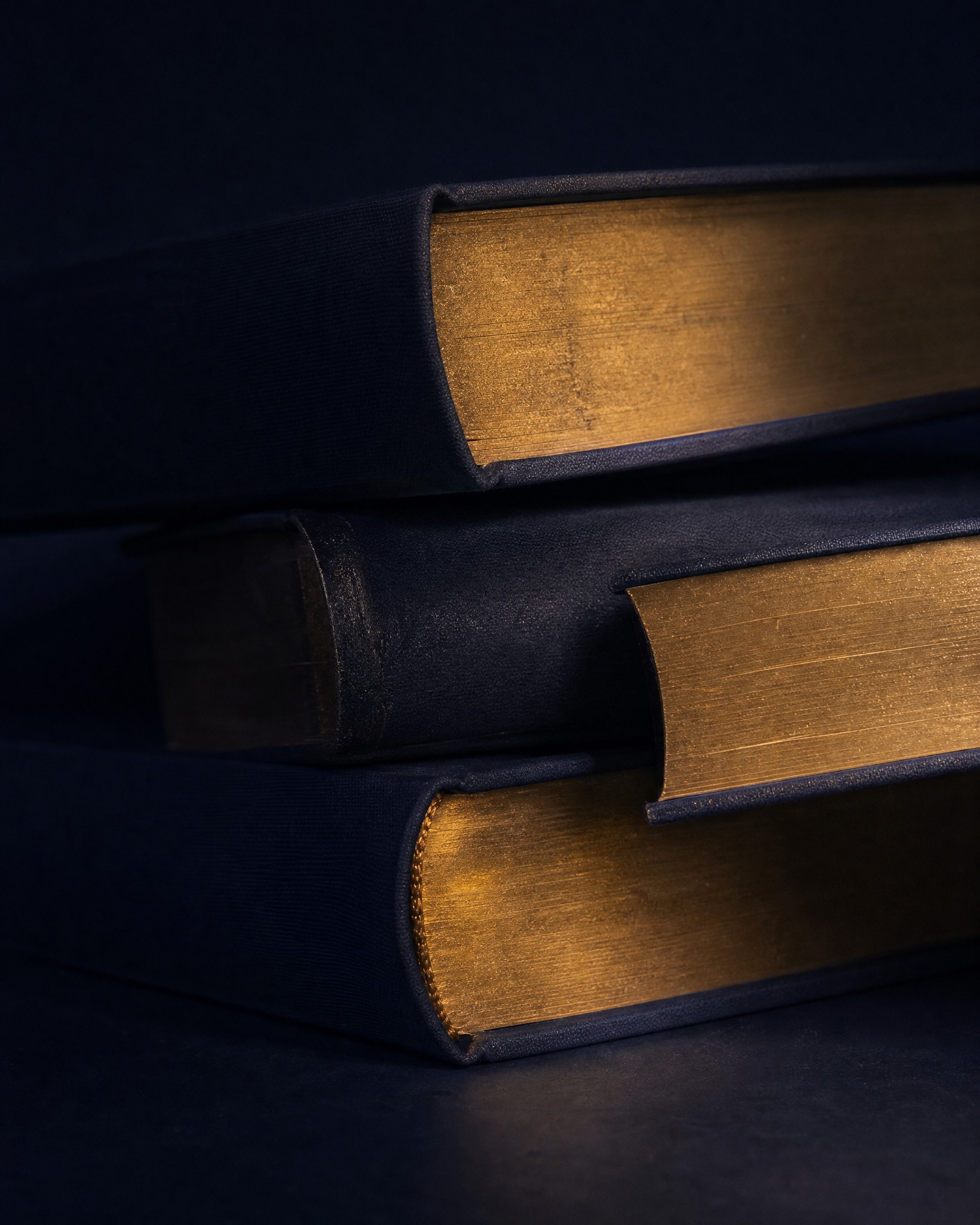 A stack of hardback books with gilded page edges catching warm light